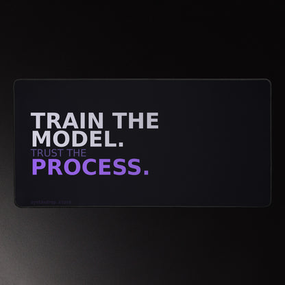 ML engineer desk mat on near-black background reading "TRAIN THE MODEL. Trust the PROCESS." in lavender-white and violet bold typography, left-anchored with wide negative space